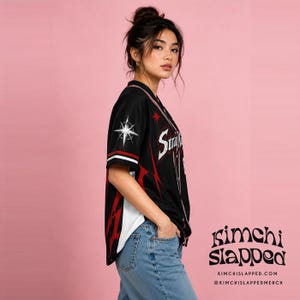 May include: A black short-sleeved button-down baseball jersey featuring red and white flame-like patterns on the sides, a white star graphic on the sleeve, and the text Stray Kids printed in white on the front chest area with a button-up closure.