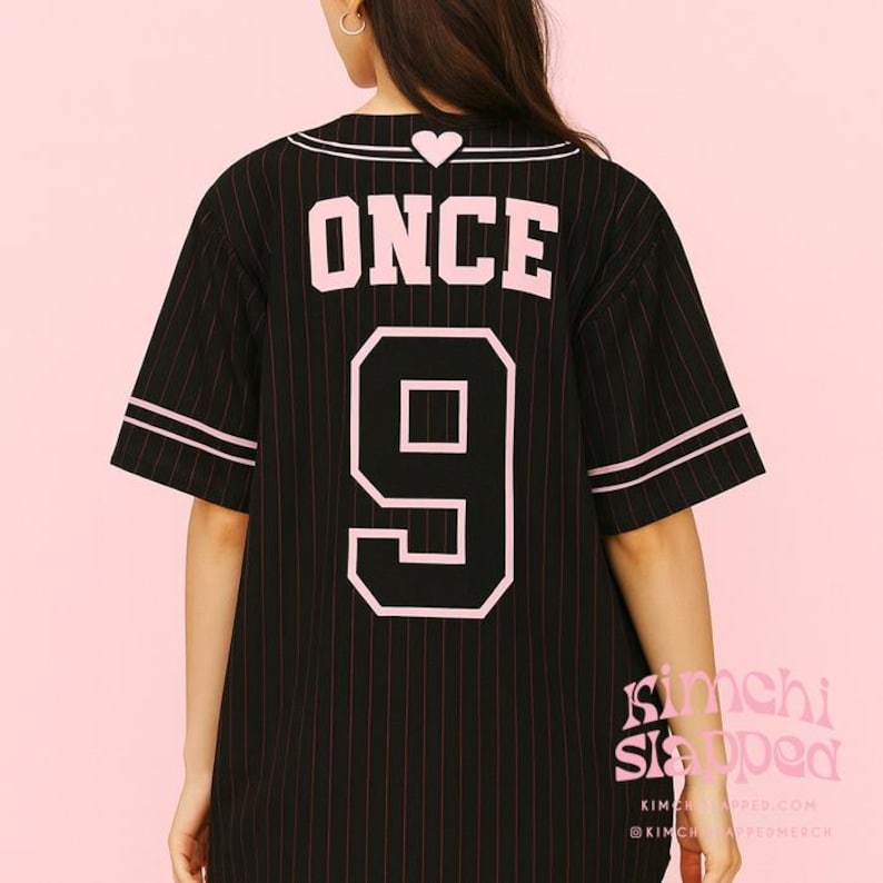 Pode incluir: Camisola de baseball preta com riscas rosa, a palavra "ONCE" e o n&uacute;mero "9" em rosa nas costas. A camisola tem acabamentos rosa nas mangas e na gola. Um pequeno cora&ccedil;&atilde;o rosa est&aacute; acima da palavra "ONCE".