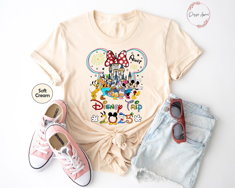 Op de afbeelding: Een cr&egrave;mekleurig T-shirt met een afbeelding van Mickey Mouse en zijn vrienden voor het kasteel van Assepoester. De tekst "Disney Trip 2023" staat onder de afbeelding. De tekst "Aunt" staat boven de afbeelding.
