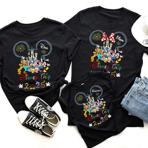 Op de afbeelding: Zwarte T-shirts met een Mickey Mouse-ontwerp met Disney-figuren en de tekst "Disney Trip 2025".
