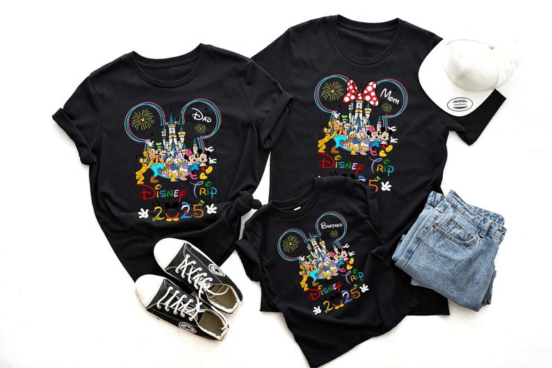 Op de afbeelding: Zwarte T-shirts met een Mickey Mouse-ontwerp met Disney-figuren en de tekst "Disney Trip 2025".