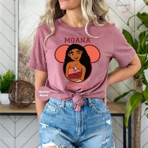May include: A heather mauve t-shirt with a graphic of Moana from the Disney movie Moana. The graphic is in a Mickey Mouse ear shape with the text "Moana Est. 2016".