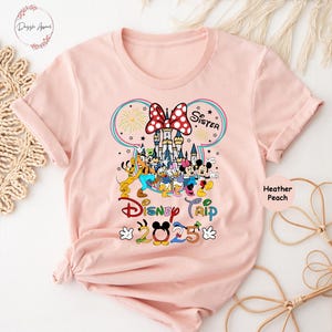 Op de afbeelding: Roze T-shirt met een afbeelding van Mickey Mouse en zijn vrienden voor het kasteel van Assepoester. De tekst "Zus" en "Disney Trip 2025" staat op het shirt.