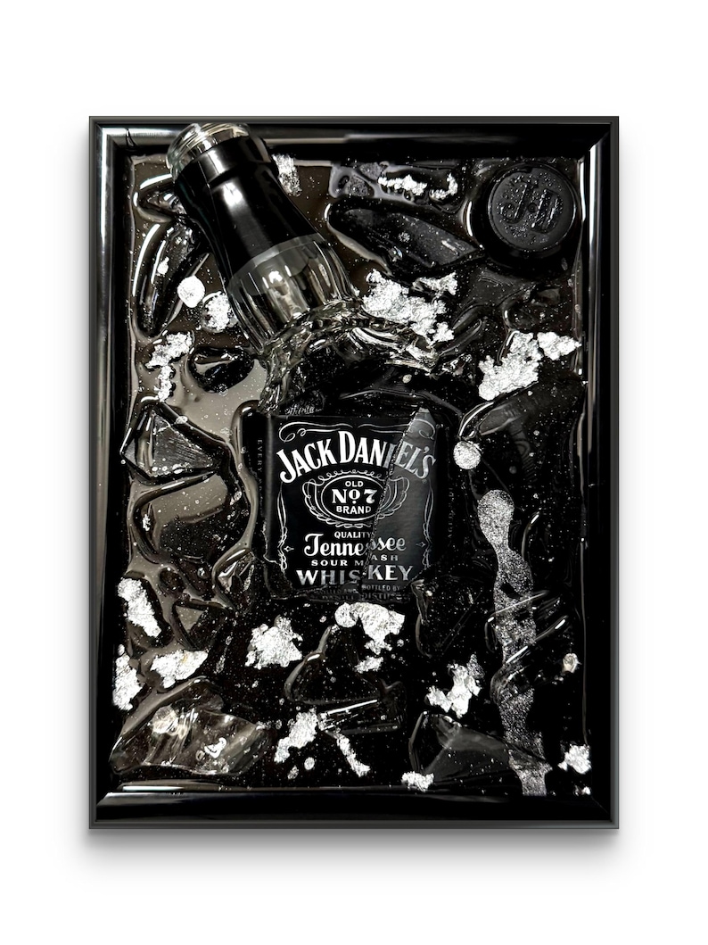 May include: Black framed artwork featuring a Jack Daniel's whiskey bottle, partially submerged in a dark liquid with silver accents. The bottle's label is prominently displayed, with the brand name and "Tennessee Sour Mash Whiskey" text.