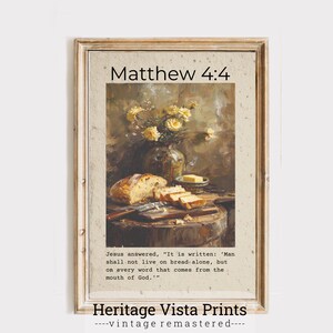 Op de afbeelding: Ingelijste vintage print met een stilleven van brood, boter en bloemen. De tekst "Matthew 4:4" staat bovenaan, met een bijbelvers eronder. De print is van Heritage Vista Prints.