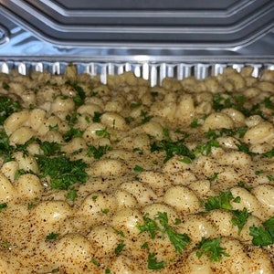 May include: A large container of creamy mac and cheese topped with fresh parsley and a sprinkle of seasoning. The container has a label that says "THE MAC".