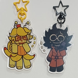 Puede incluir: Dos llaveros acrílicos con personajes de dibujos animados. Uno es amarillo con un cierre en forma de estrella, el otro es negro con un cierre en forma de estrella. El personaje amarillo tiene un diseño de plátano, y el personaje negro lleva un abrigo rojo.