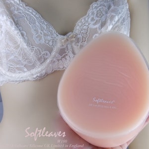 Op de afbeelding: Een close-up van een huidkleurige siliconen borstprothese met de tekst "Softleaves" en "UK (US 12) Size 6 & 4XL" gedrukt op het oppervlak. De borstprothese is gemaakt door Softcare Silicone UK Limited in Engeland.
