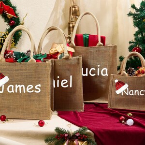 May include: Four burlap tote bags with white text and Christmas decorations. Each bag has a name: James, Daniel, Lucia, and Nancy. The bags are filled with gifts and are decorated with a Santa hat.