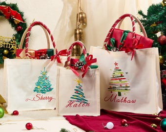 Puede incluir: Tres bolsas de lona con diseños de árboles de Navidad y nombres personalizados. Cada bolsa tiene un asa a rayas rojas y blancas y está llena de regalos. Las bolsas están decoradas con lazos y adornos rojos.