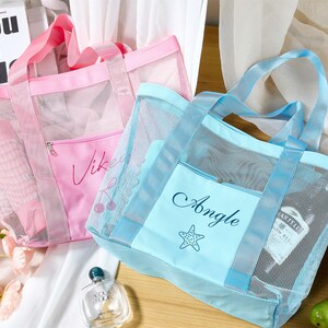 May include: Two mesh tote bags, one pink and one blue, with matching handles and front pockets. The pink bag has the name "Vikey" and a cherry design, while the blue bag says "Angle" with a starfish. Both bags are filled with items.