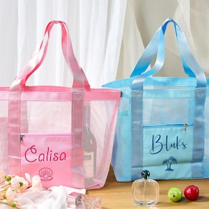 May include: Two mesh tote bags, one pink and one blue, with matching handles. The pink bag has "Calisa" embroidered on the front with a seashell design. The blue bag has "Bluks" and a palm tree design. Both have a zippered pocket.