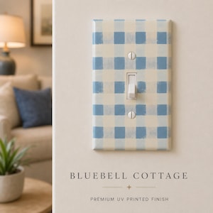 May include: A rectangular light switch wall plate featuring a blue and cream gingham check pattern. The plate has a central toggle switch and is secured with two flathead screws. The text below reads BLUEBELL COTTAGE PREMIUM UV PRINTED FINISH.