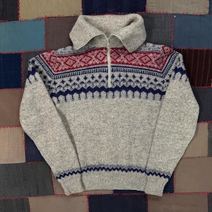 May include: A gray wool sweater with a high collar and a quarter-zip closure. The sweater features a geometric pattern in red and navy blue across the chest and sleeves. The sweater is a medium size.