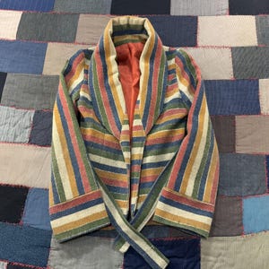 May include: A long-sleeve blazer featuring a multi-colored vertical stripe pattern in shades of blue, green, yellow, and red. The garment has a wide shawl collar, a tie-waist closure, and a solid orange interior lining visible at the front opening.