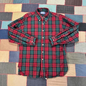 May include: A long-sleeved button-down shirt in a classic plaid pattern. The shirt features a red, green, and black color scheme. It has a button-down collar and cuffs, and a chest pocket. The shirt is made of a woven fabric.