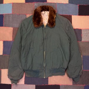 May include: Dark green bomber jacket with a brown faux fur collar. The jacket has a zipper closure and ribbed cuffs and hem. The lining is a light cream color. A vintage style jacket.