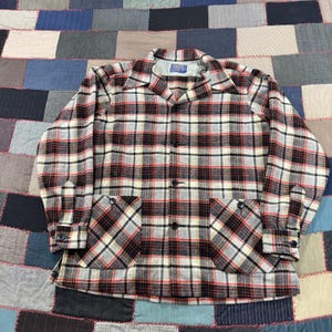 May include: A long-sleeve button-up shirt featuring a plaid pattern in black, white, gray, and red. The shirt has a pointed collar, two large front patch pockets, and buttoned cuffs. A Pendleton brand label is visible on the inside neck area.