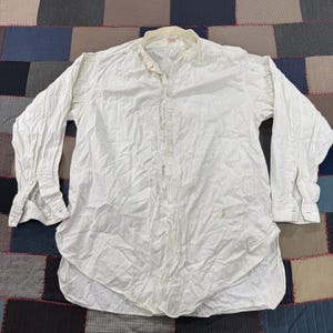 May include: A long-sleeved, off-white shirt with a mandarin collar. The shirt has a button-down front and buttoned cuffs. The fabric appears to be slightly wrinkled, and there are some light stains on the front.