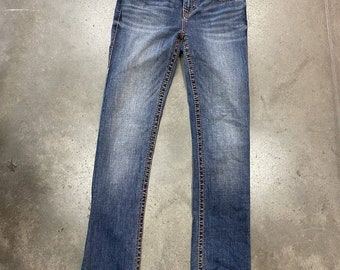 May include: A pair of blue denim jeans featuring a faded wash, a button fly closure, and prominent thick stitching along the seams and pockets. The jeans have a straight-leg cut with a classic five-pocket design and metallic hardware accents.