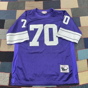 May include: A purple mesh athletic jersey featuring the number 70 in large white block lettering on the front and sleeves. The sleeves have two horizontal white stripes. A Mitchell & Ness Throwbacks label is stitched on the lower front corner.