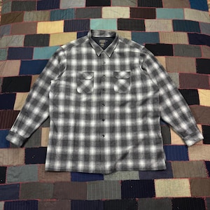 May include: A long-sleeved, button-down flannel shirt in a gray and white plaid pattern. The shirt has two chest pockets and a classic collar. The fabric appears to be a medium weight, suitable for cooler weather.