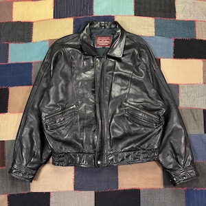 May include: Black leather jacket with a classic design. Features a collared neckline, a front zipper closure, and two zippered pockets on the chest. The jacket has a ribbed hem and cuffs. The label reads "Lord Anthony".