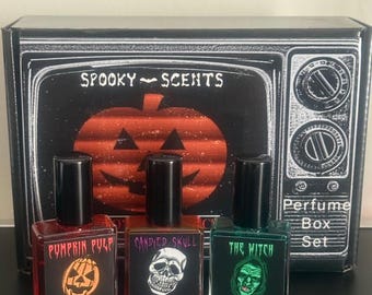 May include: A black box set labeled Spooky Scents Perfume Box Set with a vintage television graphic and a pumpkin. Three 15ml glass perfume bottles are in front: Pumpkin Pulp with orange liquid, Candied Skull with red, and The Witch with green.
