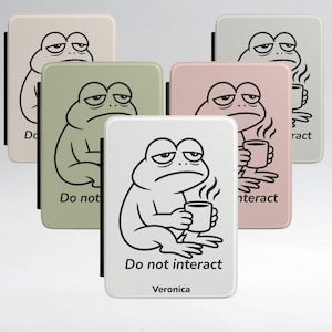 May include: A collection of rectangular phone cases in various pastel colors, each featuring a black and white cartoon frog with a grumpy expression. The frog is holding a coffee cup, and the text "Do not interact" is printed on the cases.