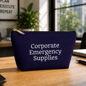 Peut inclure: Une pochette zippée bleu marine foncé avec le texte blanc Corporate Emergency Supplies imprimé sur le devant. La pochette possède une tirette de fermeture éclair en métal doré et une forme trapézoïdale structurée avec une base plate.