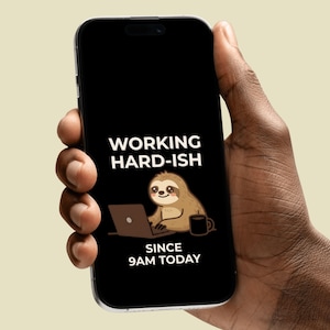 Può includere: Uno smartphone nero mostra il testo "WORKING HARD-ISH SINCE 9AM TODAY" con un bradipo dei cartoni animati che usa un laptop e una tazza di caffè. Il telefono è tenuto in una mano.