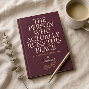 May include: A burgundy journal with the text "THE PERSON WHO ACTUALLY RUNS THIS PLACE" in white. The journal includes the text "A PERSONAL RECORD" and "by Caroline". A gold pen and a cup of coffee are also present.
