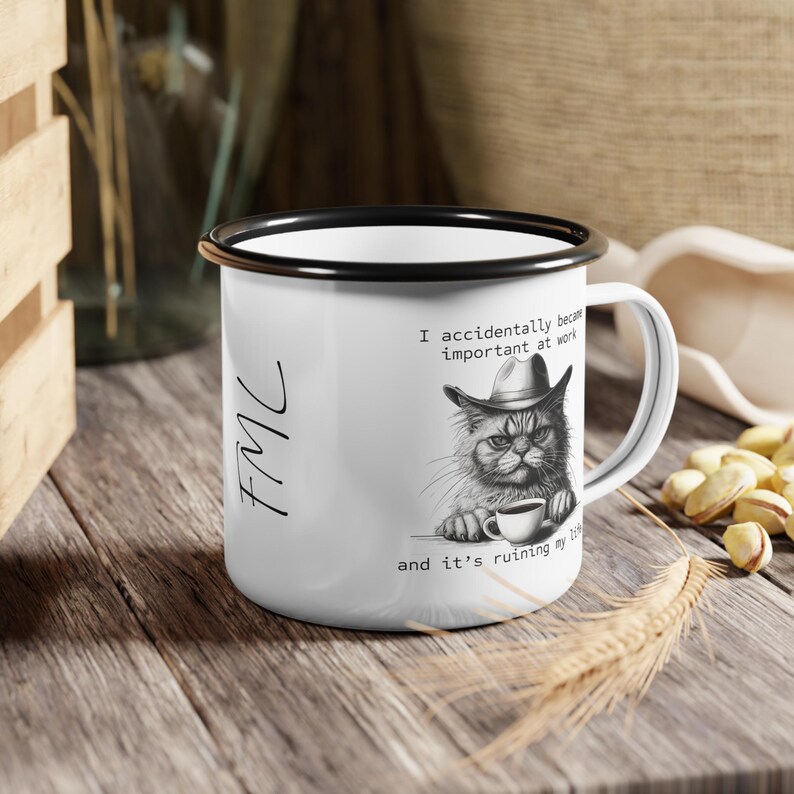 May include: White enamel mug with a black rim and handle. The mug features a black and white illustration of a cat wearing a hat and holding a coffee cup, with the text "I accidentally became important at work and it's ruining my life."