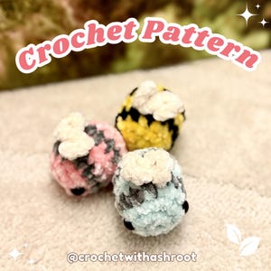 May include: Three small plush crochet bee figures with white wings and black eyes. One is yellow and black, one is pink and gray, and one is light blue and gray. The text Crochet Pattern is at the top and @crochetwithashroot is at the bottom.