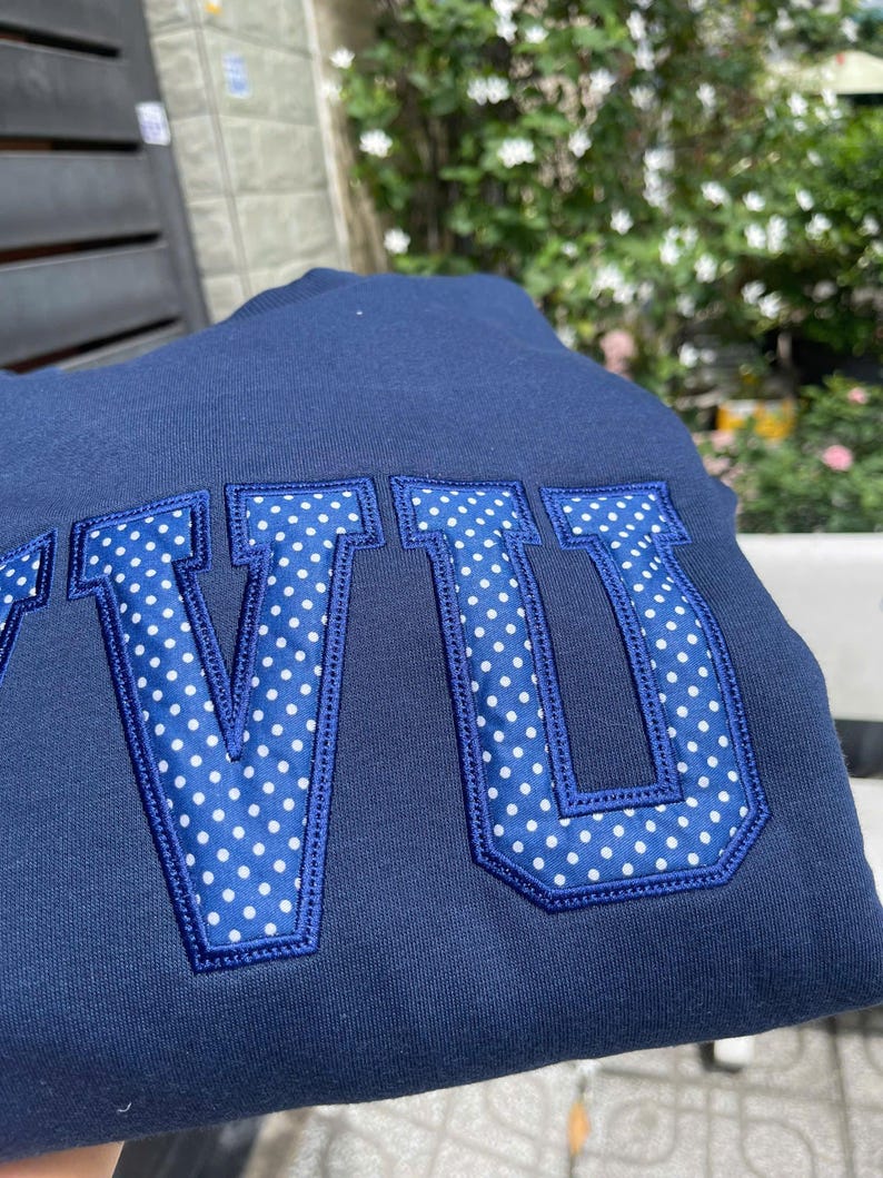 Puede incluir: Sudadera azul marino con las letras "VU" en tela de lunares blancos. Las letras est&aacute;n delineadas en azul marino y cosidas a la sudadera. El fondo es azul marino liso.
