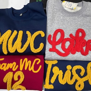 Puede incluir: Cuatro sudaderas en azul marino, gris y burdeos. La sudadera azul marino tiene "MWC" en amarillo, la gris "Lake" en rojo, la burdeos "Team MC 12" en amarillo y la azul marino "Irish" en amarillo.