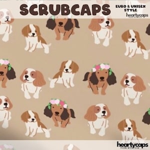 May include: A tan background with a repeating pattern of brown and white Cavalier King Charles Spaniel dogs. Some of the dogs are wearing floral headbands. The text "SCRUBCAPS" is at the top of the image. The text "EURO & UNISEX STYLE" is in the top right corner of the image. The text "heartycaps" is in the bottom right corner of the image.