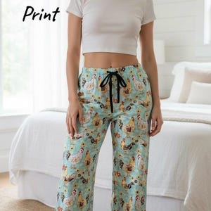 May include: A woman wearing a white crop top and light blue pajama pants. The pajama pants have a repeating pattern of chickens and sunflowers. The text "Chicken Mom Print" is in the upper left corner.