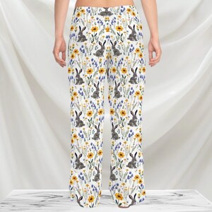 May include: White pajama pants with a repeating pattern of gray rabbits, yellow sunflowers, and blue wildflowers. The pants have a wide leg design and are made of a soft, lightweight fabric.