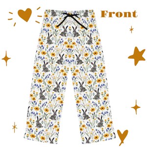 May include: White pajama pants with a floral and bunny rabbit pattern. The pants feature a drawstring waist and are covered in yellow flowers, blue wildflowers, and gray bunnies. The word "Front" is printed on the top right.