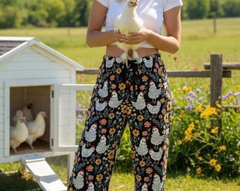 May include: Black pajama pants with a white chicken and floral pattern. A white hen is held in front of the pants. A white chicken coop is in the background.