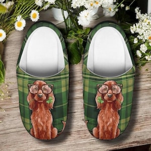 May include: A pair of slip-on slippers featuring a green and black plaid pattern. Each slipper displays a graphic illustration of a brown Irish Setter dog wearing brown-rimmed glasses and holding a green shamrock in its mouth.
