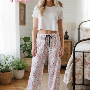 Könnte beinhalten: Weiße Schlafanzughose mit rosa Ferkel- und Blumenmuster, kombiniert mit einem weißen Crop-Top. Die Hose hat einen schwarzen Kordelzug. Der Text "Piglet Print" ist in rosa Buchstabenblasen.
