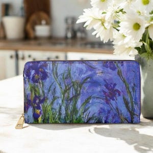 May include: A rectangular zip-around wallet featuring an impressionist-style print of purple and blue iris flowers with green stems and leaves against a textured blue background. The wallet has a gold-toned metal zipper pull on the left side.
