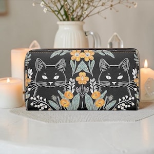 May include: Black wallet with a zipper closure, featuring a repeating pattern of black cat faces, yellow flowers, and green leaves on a black background. The wallet is rectangular and appears to be made of leather or a similar material.