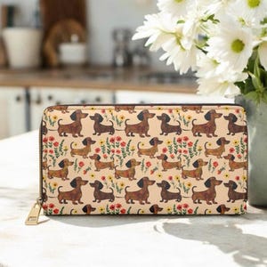 Op de afbeelding: Een beige portemonnee met ritssluiting met een herhalend patroon van bruine teckel honden en kleurrijke bloemen. De portemonnee heeft een goudkleurige rits en trekker en is waarschijnlijk gemaakt van duurzaam materiaal.