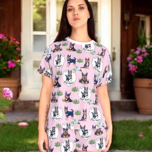 May include: Pink pajama set featuring a repeating pattern of Australian Cattle Dogs, also known as Blue Heelers, and the text "Aus Blue Heeler". The set includes a short-sleeved top and matching shorts. The top has a white collar.