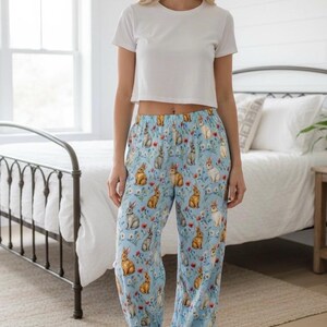 Puede incluir: Pantalones de pijama azul claro con un estampado repetido de conejos y flores. Los pantalones se combinan con un top corto blanco. Los pantalones de pijama están hechos de una tela suave y ligera.