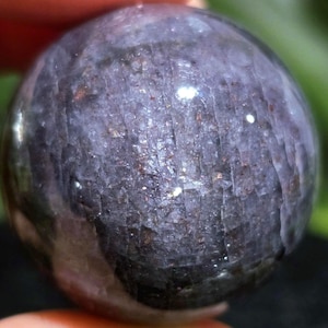 Sunstone Iolite Sphere with Purple hue and sparkling rainbow confetti flash on hand.