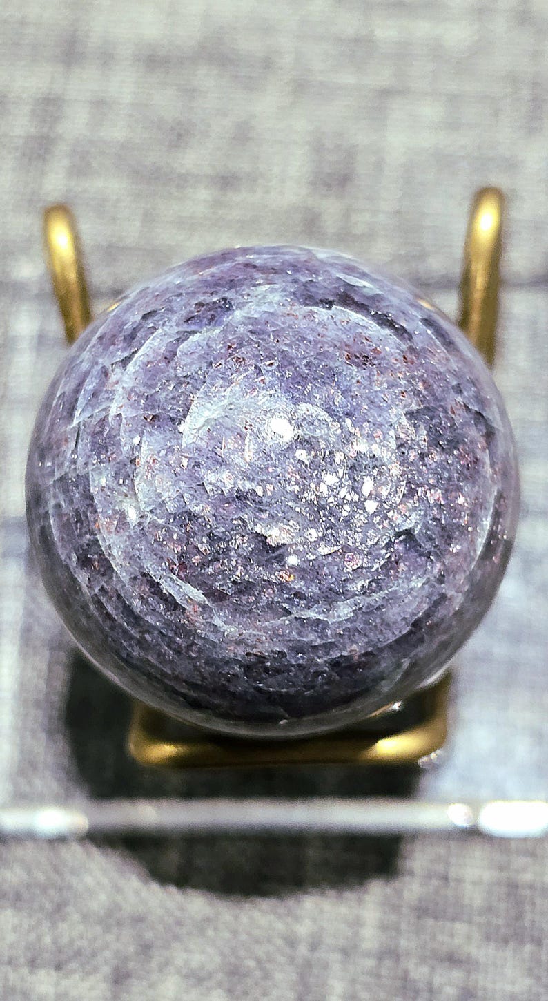 May include: A purple and silver sphere with a swirling pattern, displayed on a gold stand.